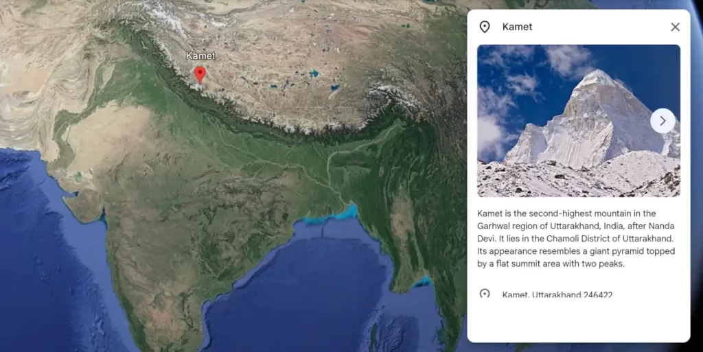 A Google Maps image of Mount Kamet, the third-highest mountain in India and the 28th-highest mountain in the world. The mountain is located in the Garhwal Himalayas of India. The summit is covered in snow and ice, and the surrounding peaks are shrouded in clouds. The image shows the mountain from a distance, and the surrounding area is sparsely populated.
